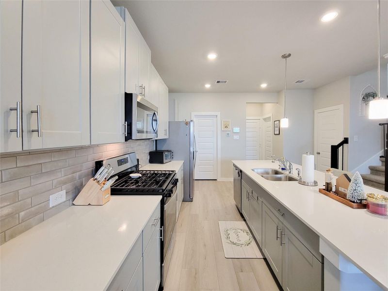 This modern kitchen features sleek white cabinets, stainless steel appliances, and a spacious island with a double sink. The neutral backsplash complements the light wood flooring, creating a bright and inviting space.