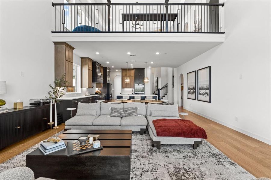 Living room featuring light wood finished floors, a towering ceiling, arched walkways, recessed lighting, and stairway Living room featuring light wood finished floors, a towering ceiling, arched walkways, recessed lighting, and stairway