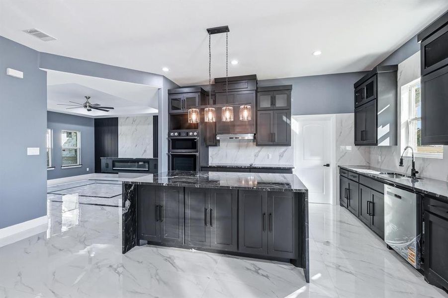 Kitchen featuring dark stone counters, light marble finish floors, a ceiling fan, a spacious island, and recessed lighting