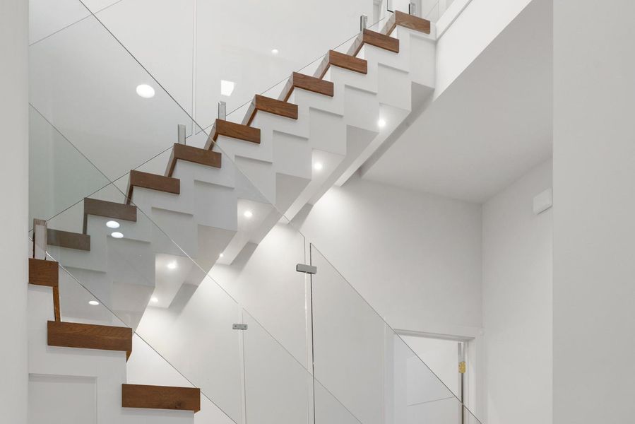 Modern staircase featuring hardwood treads, clear glass railings, and integrated lighting