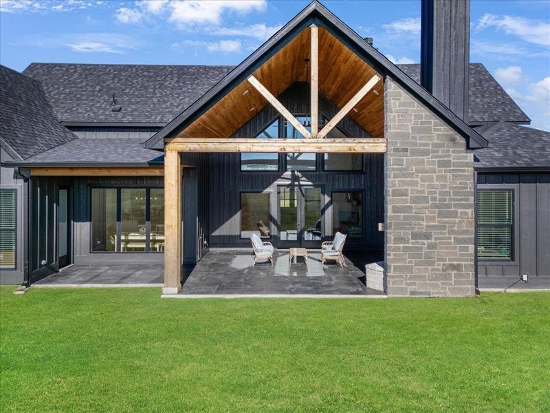 Rear view of property with a shingled roof, a patio area, board and batten siding, and a lawn