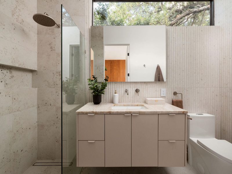 Natural stone textures and integrated glass shower define this contemporary bath space.