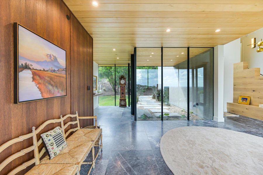 Entryway featuring a wall of windows, wooden walls, wood ceiling, and stairs