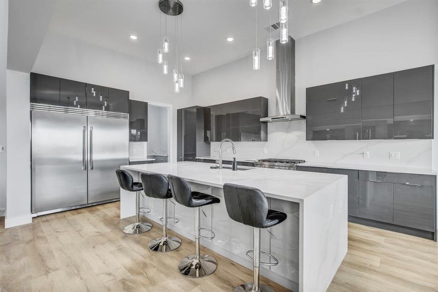 Kitchen with modern cabinets, decorative light fixtures, a breakfast bar area, stainless steel built in refrigerator, and a center island with sink