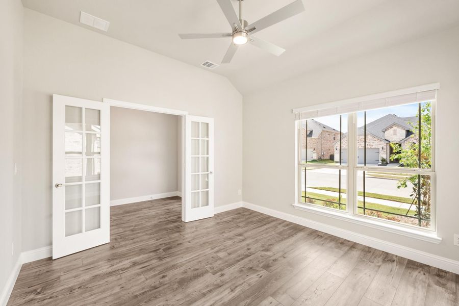 Empty room with vaulted ceiling, ceiling fan, French doors, and large windows with hardwood floors