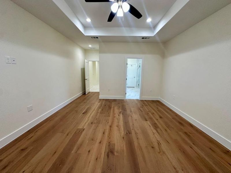 Unfurnished bedroom featuring wood finished floors, a tray ceiling, a ceiling fan, and recessed lighting