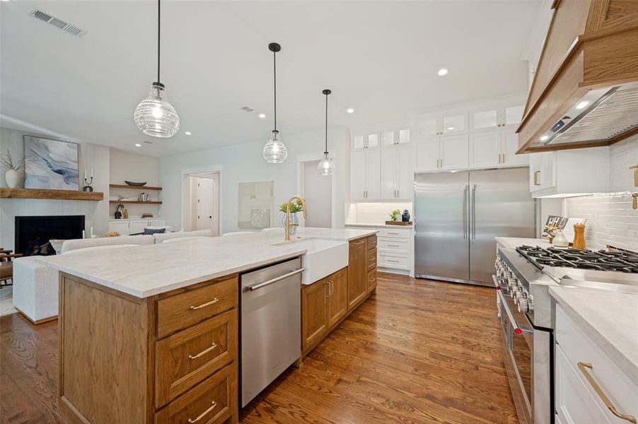 Gourmet kitchen with wood-finish flooring, a large center island, farmhouse sink, stainless steel appliances, and abundant white cabinetry