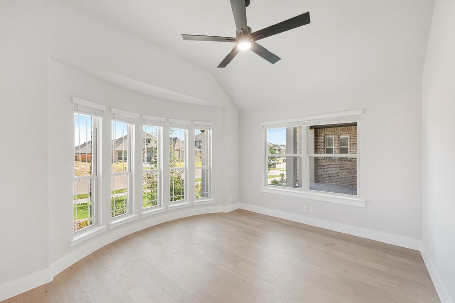 Empty bedroom with vaulted ceiling, ceiling fan, hardwood floors, and large windows with neighborhood views Empty bedroom with vaulted ceiling, ceiling fan, hardwood floors, and large windows with neighborhood views