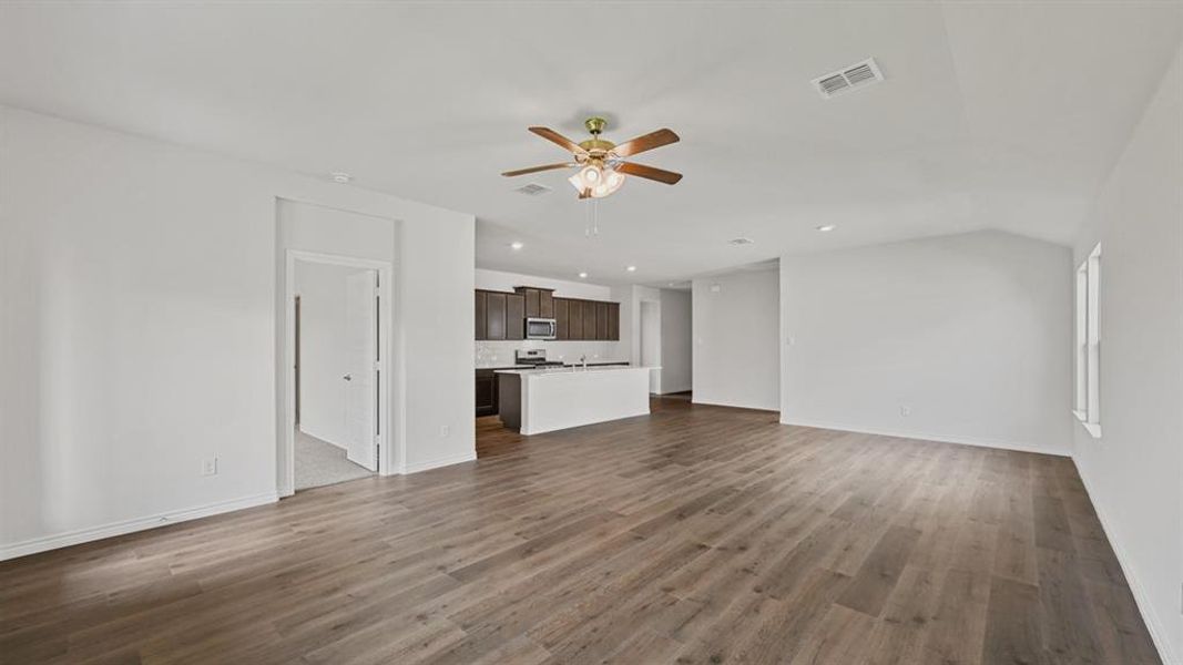Spacious open-concept living area featuring wood-finish flooring, vaulted ceilings, and a ceiling fan with integrated lighting Spacious open-concept living area featuring wood-finish flooring, vaulted ceilings, and a ceiling fan with integrated lighting