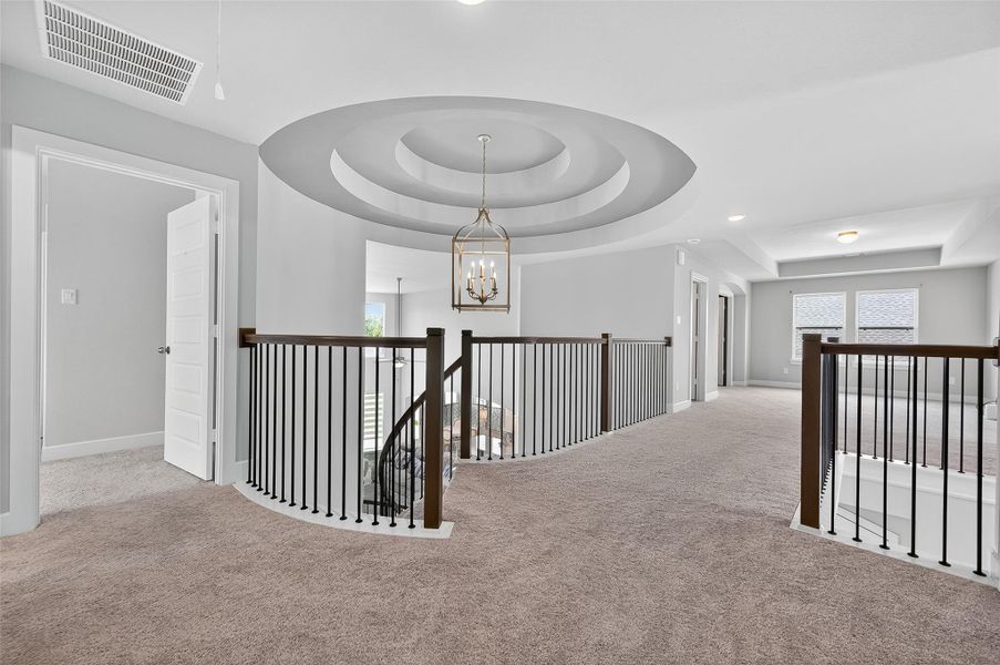 Beautiful upstairs landing features a grand rotunda ceiling with layered detailing and a modern chandelier. The open layout is accented by wrought iron railings and plush carpeting, offering a smooth transition between rooms.