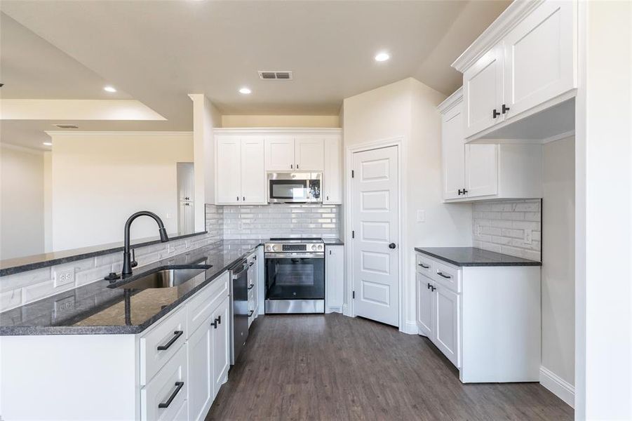Modern kitchen featuring white shaker cabinetry, dark granite-style countertops, a subway tile backsplash, stainless steel appliances, and wood-finish flooring