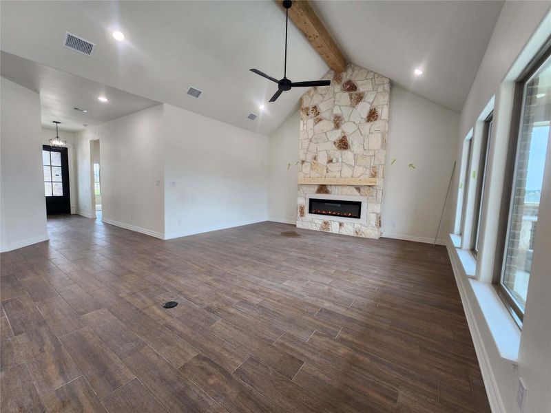 Spacious living area featuring wood-finish tile flooring, a vaulted ceiling with exposed beam, an electric fireplace with stone surround, a wood mantel, and multiple recessed lights