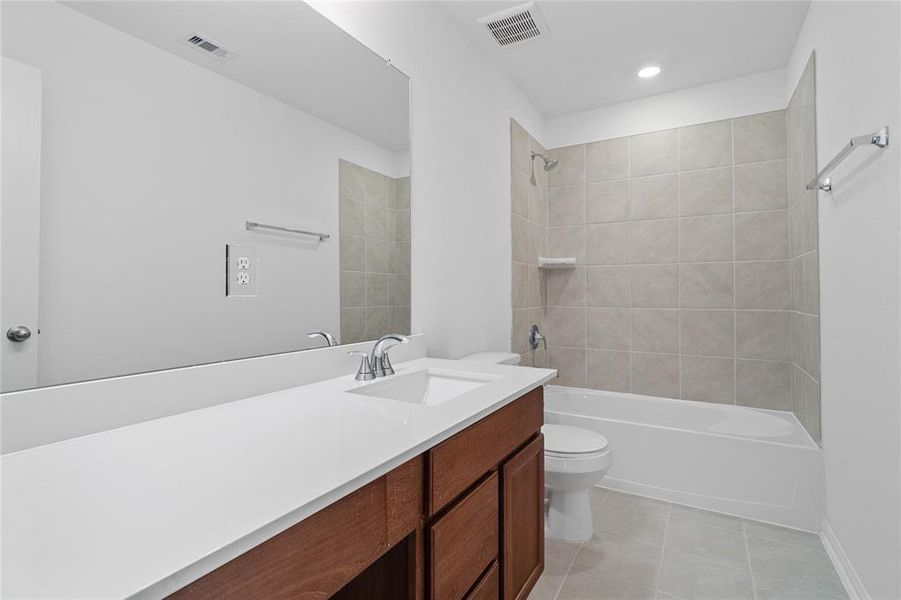 Secondary bath features tile flooring, bath/shower combo with tile surround, stained wood cabinets, beautiful light countertops, mirror, sleek fixtures and modern finishes.