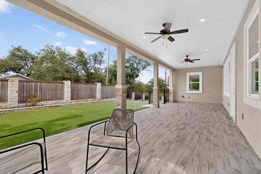 An expansive covered patio features wood-look tile flooring and recessed lighting overlooking a manicured yard.