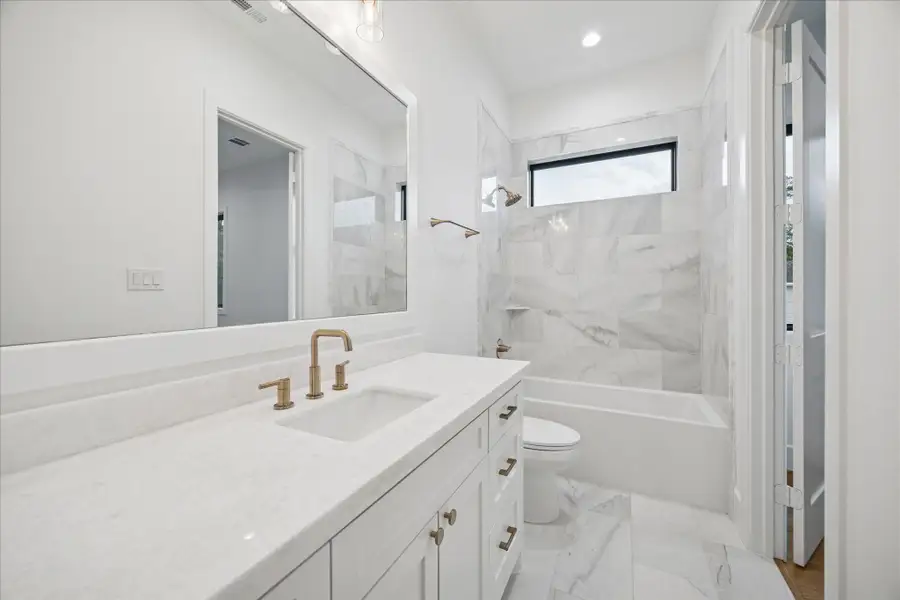 Soft neutral tones, polished tile, and warm brass accents create a refined, modern atmosphere in this secondary en-suite bath.