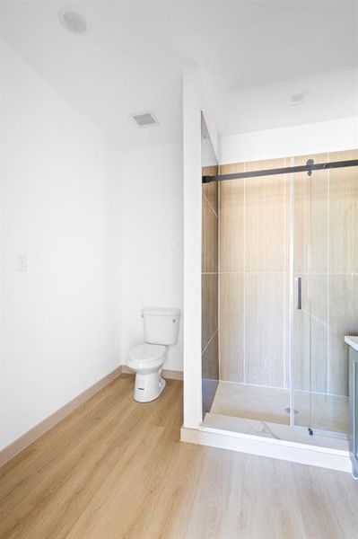 Bathroom with a shower stall, wood finished floors, visible vents, toilet, and baseboards Bathroom with a shower stall, wood finished floors, visible vents, toilet, and baseboards