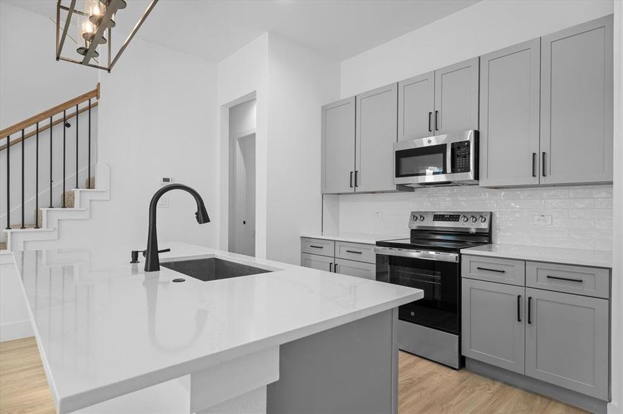 Kitchen featuring gray cabinetry, stainless steel appliances, light wood-style flooring, tasteful backsplash, and light stone countertops Kitchen featuring gray cabinetry, stainless steel appliances, light wood-style flooring, tasteful backsplash, and light stone countertops