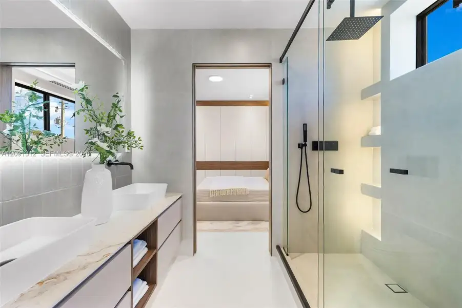 Floating dual vanity with stone-surfaced countertop, rectangular vessel sinks, matte black fixtures, walk-in glass-enclosed shower with built-in recessed shelving, and large-format wall tiling Floating dual vanity with stone-surfaced countertop, rectangular vessel sinks, matte black fixtures, walk-in glass-enclosed shower with built-in recessed shelving, and large-format wall tiling