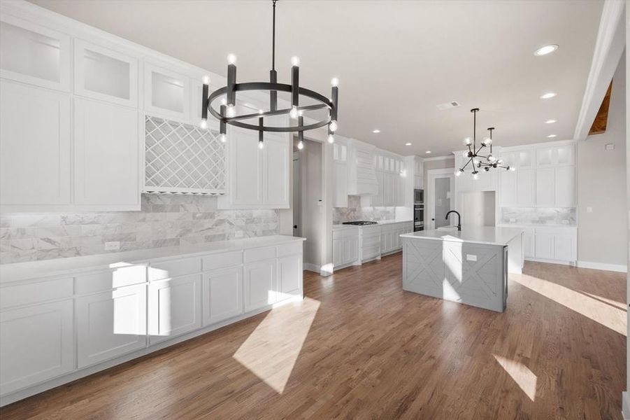 Kitchen featuring an island with sink, a notable chandelier, and white cabinetry