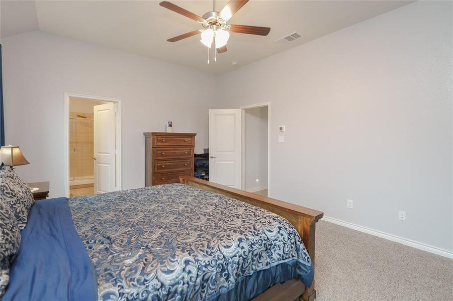 Bedroom featuring carpet flooring, vaulted ceiling, ensuite bath, and ceiling fan