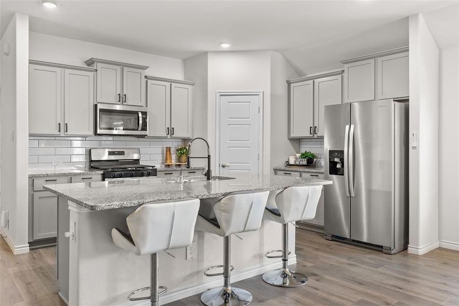 Kitchen with stainless steel appliances, light stone counters, tasteful backsplash, gray cabinetry, and a breakfast bar area Kitchen with stainless steel appliances, light stone counters, tasteful backsplash, gray cabinetry, and a breakfast bar area