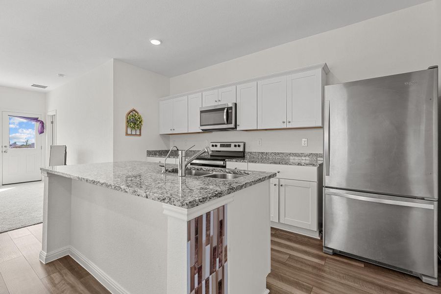 Kitchen featuring stainless steel appliances, white cabinetry, light stone counters, a center island with sink, and recessed lighting Kitchen featuring stainless steel appliances, white cabinetry, light stone counters, a center island with sink, and recessed lighting
