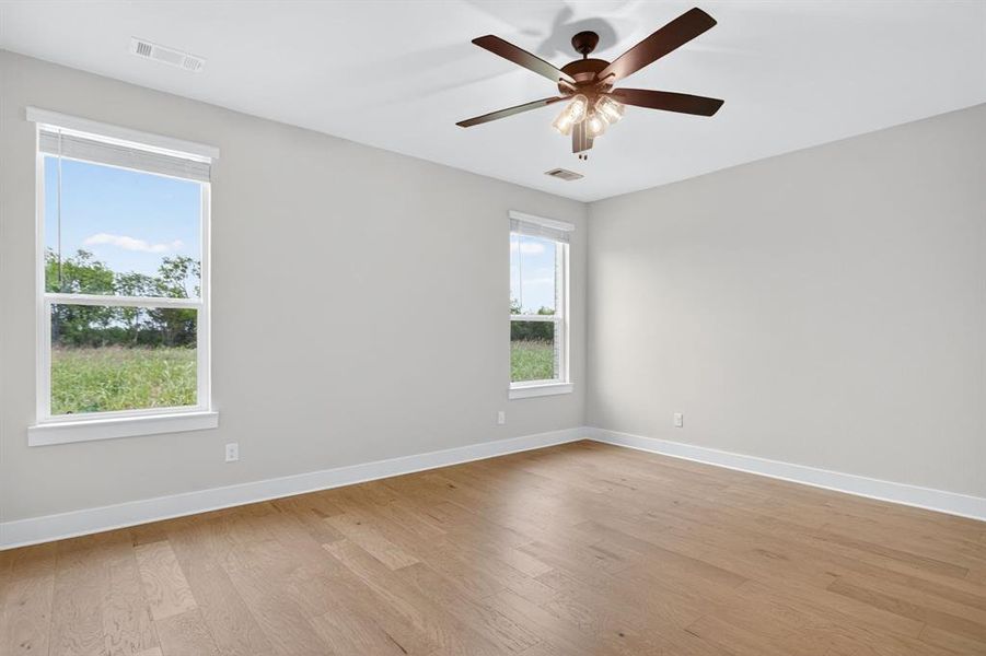 Spacious room featuring wood-finish flooring, light gray walls, white trim, and a ceiling fan with integrated lighting Spacious room featuring wood-finish flooring, light gray walls, white trim, and a ceiling fan with integrated lighting