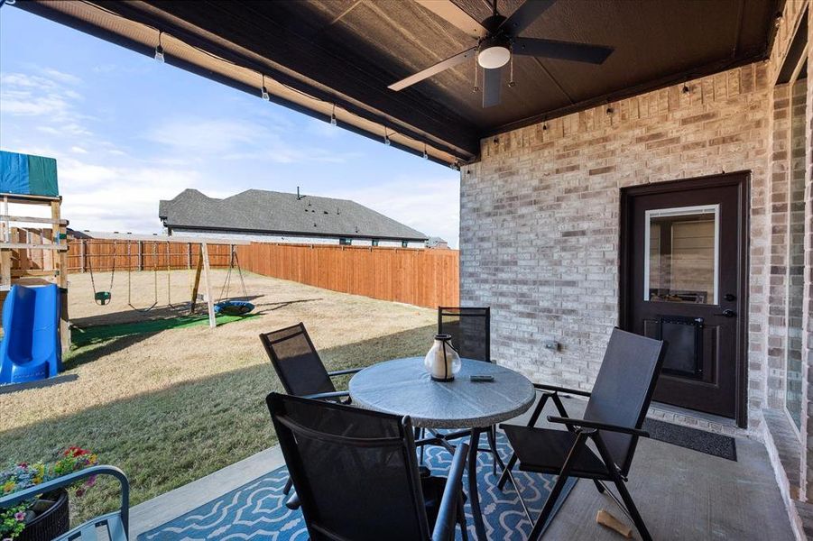 Fenced backyard featuring a playground, a patio, outdoor dining space, and a ceiling fan
