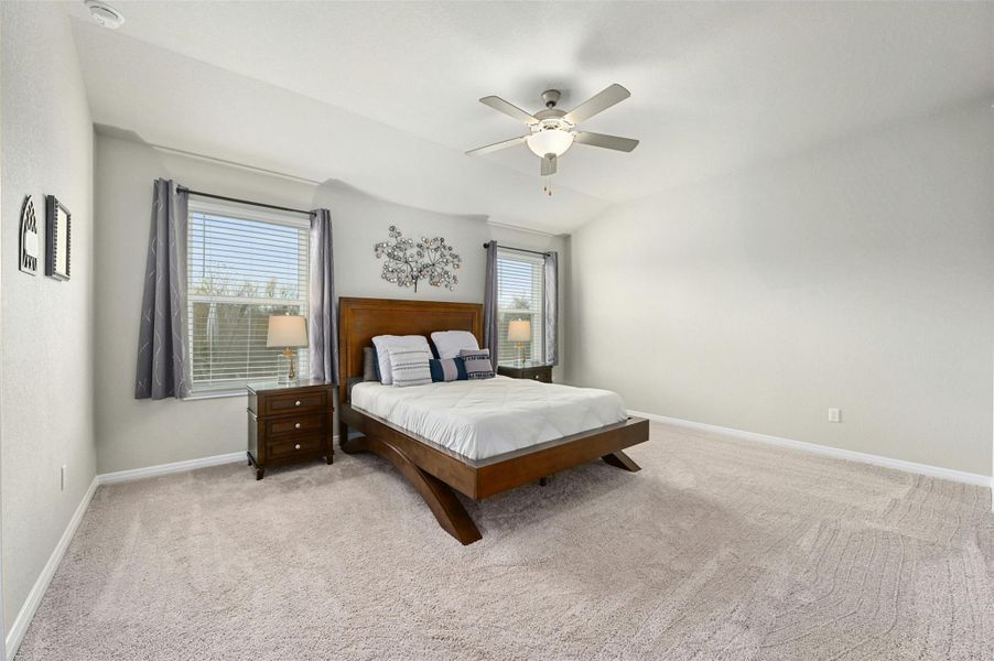 Carpeted bedroom featuring ceiling fan, vaulted ceiling, and multiple windows