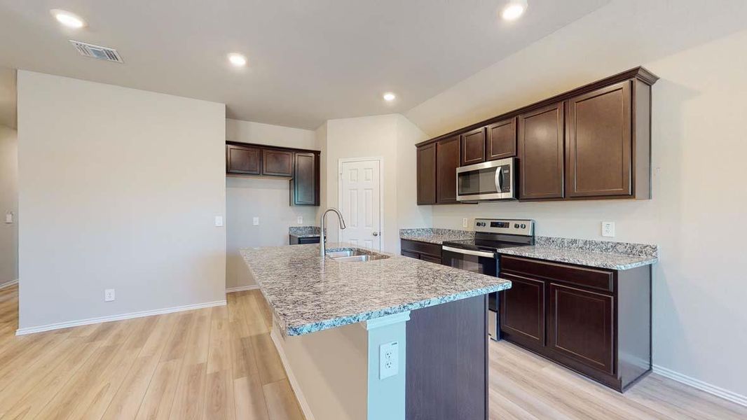 Open concept kitchen featuring an island with a stainless steel sink, granite countertops, wood-finish flooring, dark wood cabinetry, and stainless steel appliances