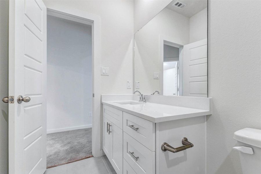 Another view of the bathroom highlights the white vanity, modern hardware, chrome faucet, and spacious countertop. The large mirror helps the room feel open and bright, while the nearby doorway connects easily to the bedroom, making this bathroom both practical and convenient for everyday use. Another view of the bathroom highlights the white vanity, modern hardware, chrome faucet, and spacious countertop. The large mirror helps the room feel open and bright, while the nearby doorway connects easily to the bedroom, making this bathroom both practical and convenient for everyday use.