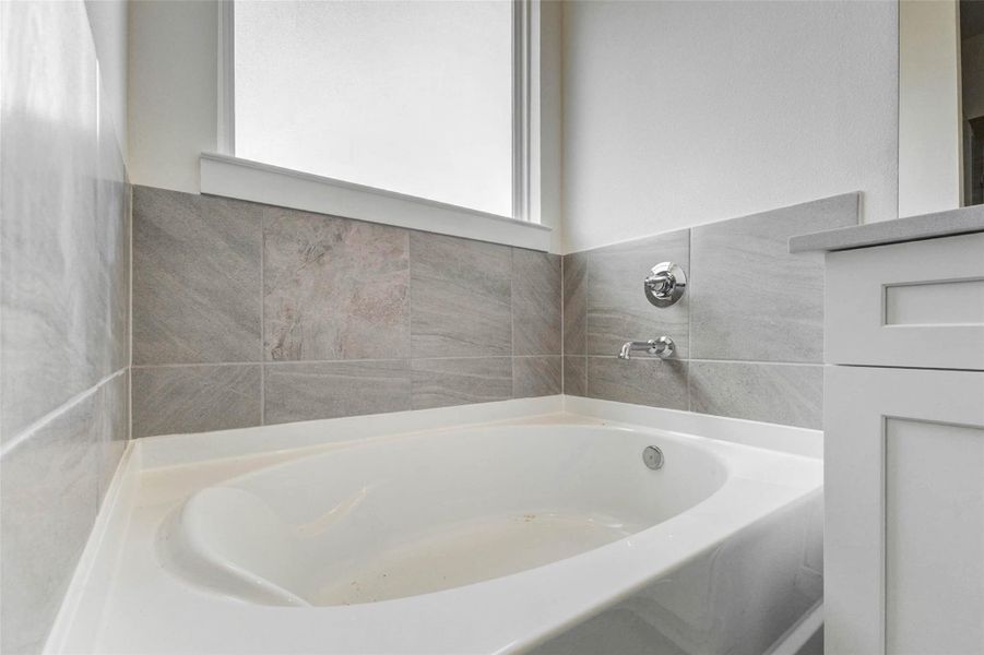 Close-up of the soaking tub framed by neutral tile surround, natural light, and nearby vanity. This relaxing bath feature provides a comfortable place to unwind, while the clean tilework, chrome fixtures, and bright window add a fresh, spa-like touch to the primary bathroom.