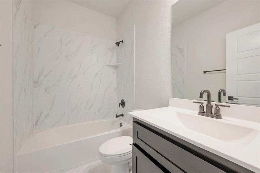 Bathroom featuring a white tub with a white-toned, patterned surround, a dark-toned vanity cabinet, a white countertop with an integrated sink, and dark-toned fixtures Bathroom featuring a white tub with a white-toned, patterned surround, a dark-toned vanity cabinet, a white countertop with an integrated sink, and dark-toned fixtures