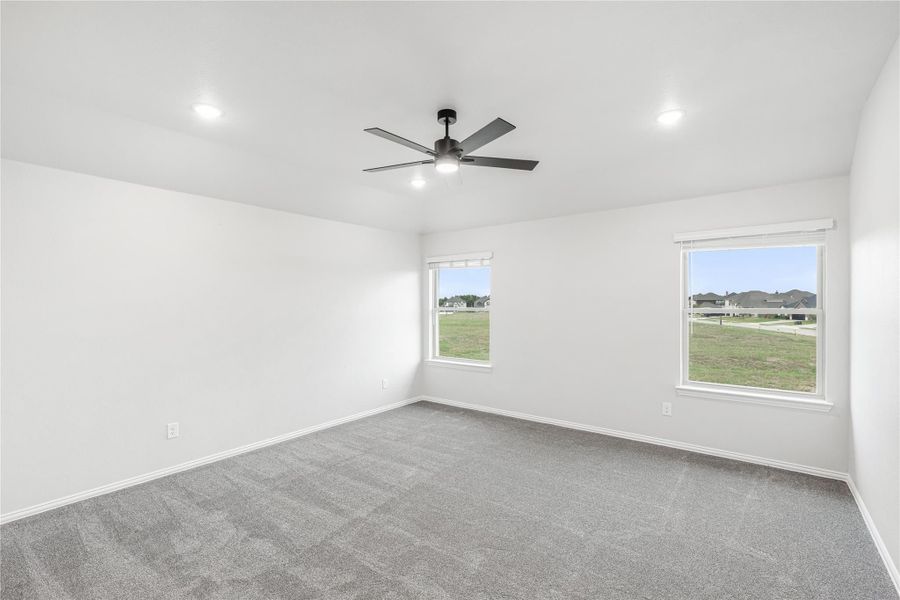 Empty bedroom with gray carpet, ceiling fan, and two windows overlooking a neighborhood