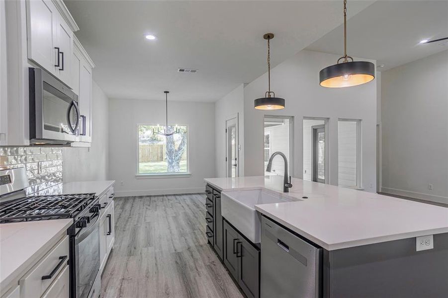 Kitchen with appliances with stainless steel finishes, decorative light fixtures, light wood-type flooring, an island with sink, and white cabinetry