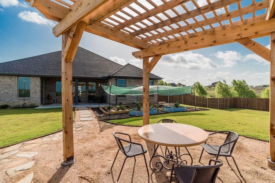 Expansive backyard featuring a covered patio extended to a wooden pergola living space, vegetable garden, a large grassy area, and a privacy fence.