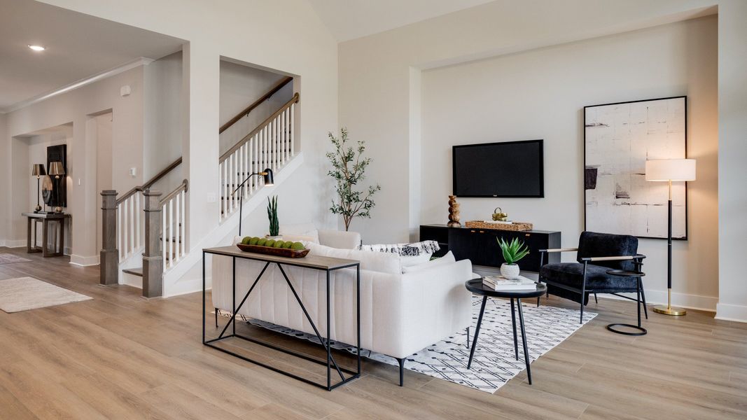 Large living room area with vaulted ceiling next to staircase and kitchen