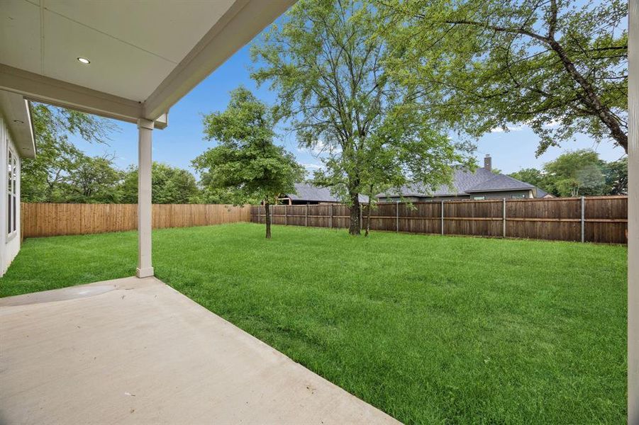 Covered back patio opening to a spacious fenced backyard with mature trees