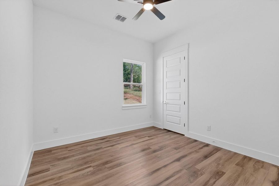 A well-lit bedroom features durable hardwood-style flooring and a functional ceiling fan for comfort.