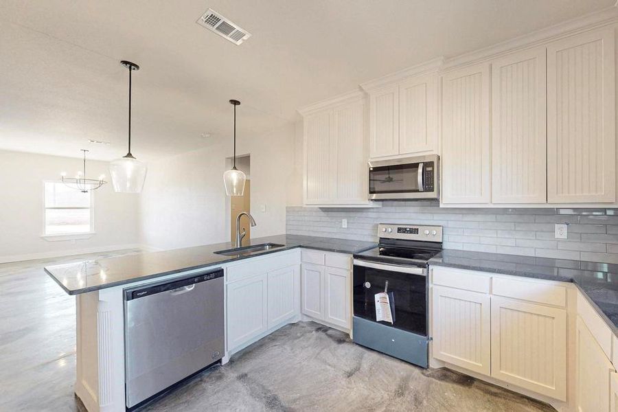 Kitchen featuring stainless steel appliances, a peninsula, a sink, visible vents, and decorative backsplash