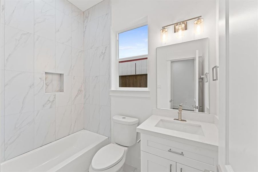 Modern bathroom with a clean, bright design. Features include a white vanity with a sleek faucet, a large mirror, and a bathtub with elegant marble-patterned tiles. There's a window for natural light and stylish lighting fixtures above the mirror.