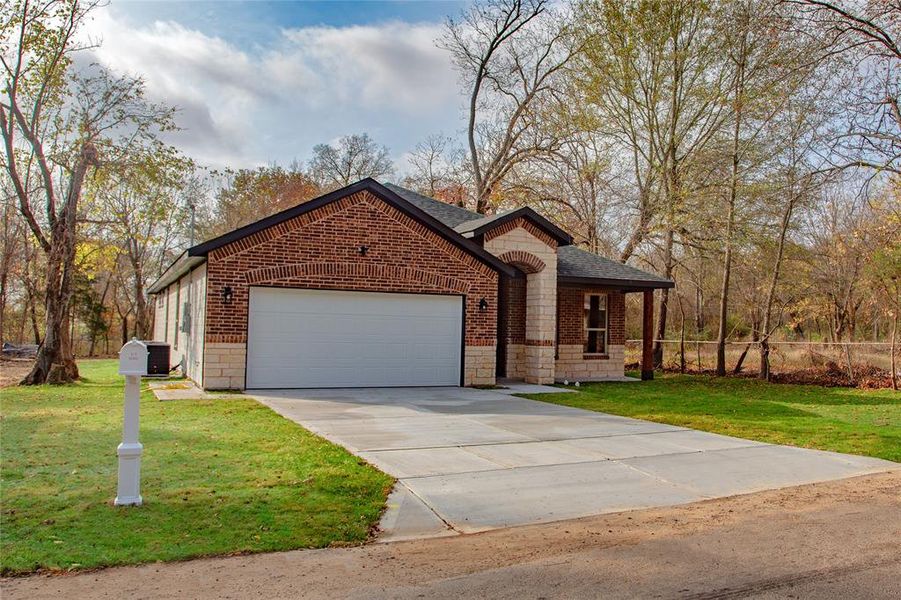 Single story home with stone siding, driveway, an attached garage, roof with shingles, and brick siding