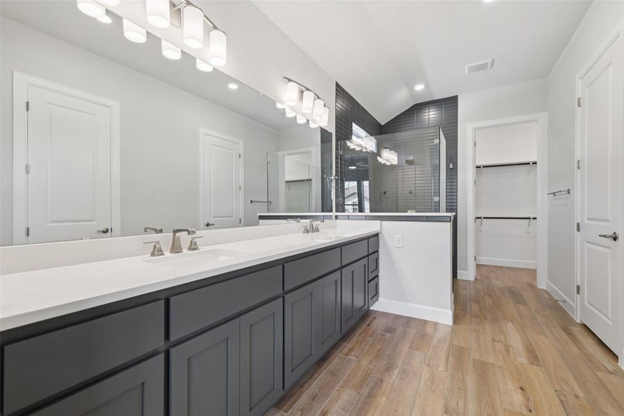 Full bathroom featuring double vanity, a tile shower, vaulted ceiling, wood finished floors, and a walk in closet