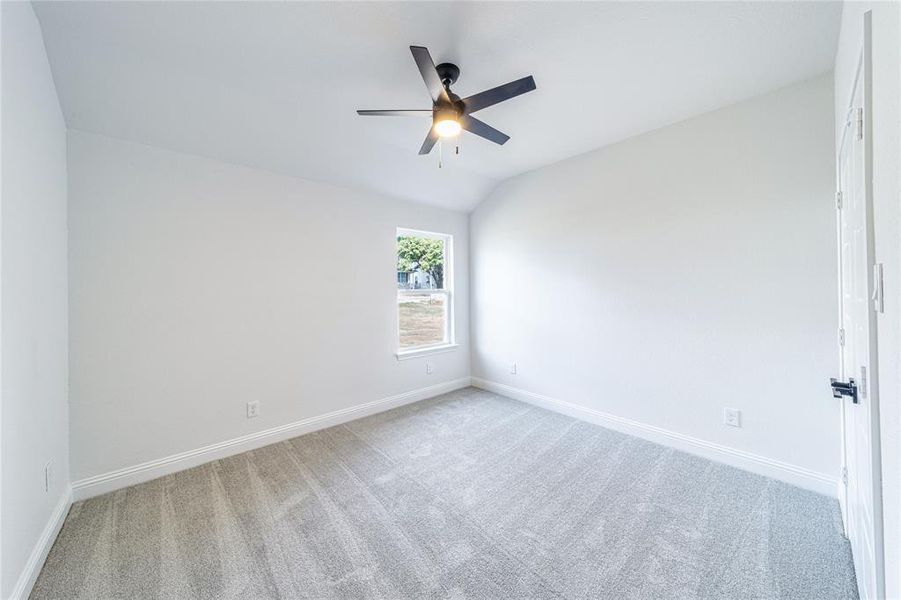 Carpeted empty room featuring vaulted ceiling, a ceiling fan, and baseboards