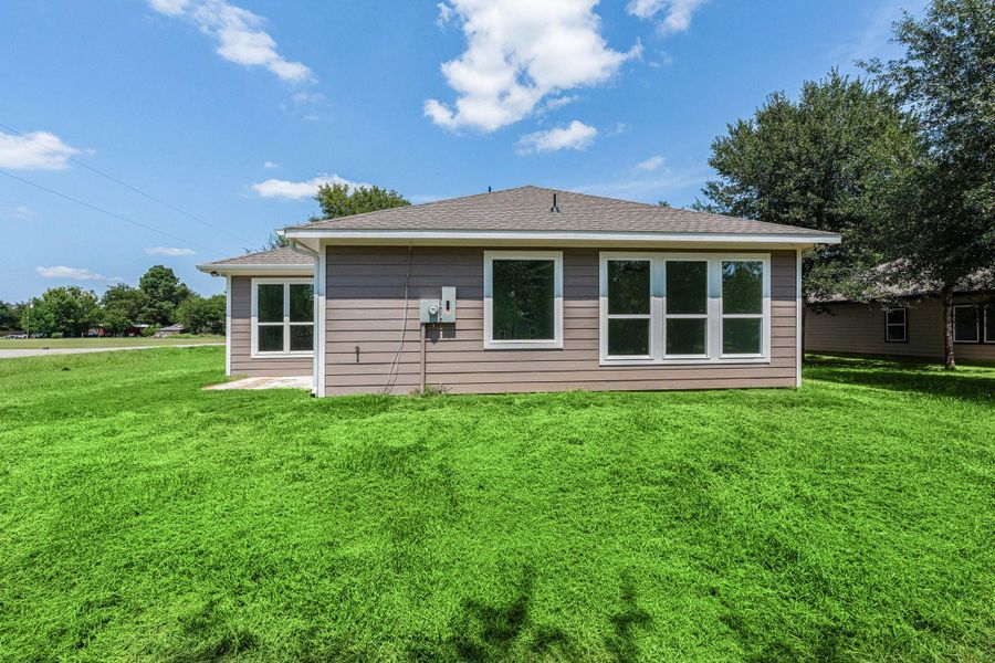 This photo shows the back view of a single-story home with a well-maintained lawn. The house features a neutral exterior and large windows, allowing for ample natural light. It is situated on a spacious corner lot with surrounding greenery and a clear blue sky overhead. This photo shows the back view of a single-story home with a well-maintained lawn. The house features a neutral exterior and large windows, allowing for ample natural light. It is situated on a spacious corner lot with surrounding greenery and a clear blue sky overhead.