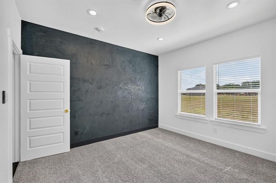 Room featuring a textured accent wall, two windows with blinds, a ceiling fan with integrated lighting, recessed lighting, and grey carpet flooring