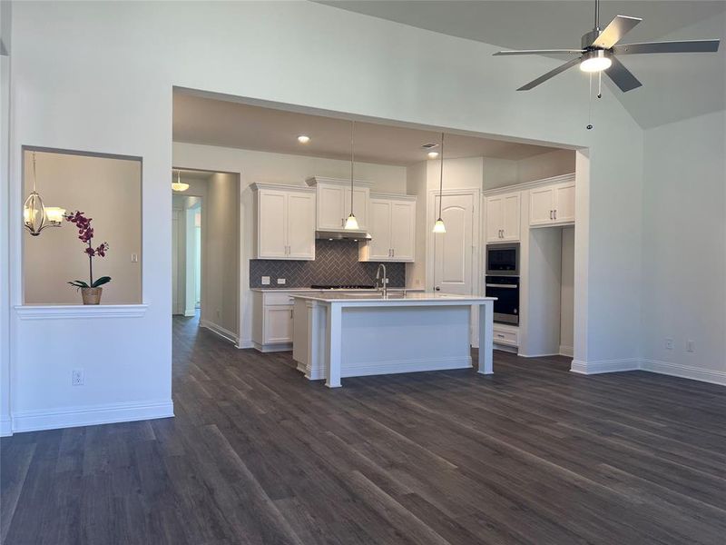 Kitchen featuring dark wood-style floors, a center island with sink, stainless steel appliances, tasteful backsplash, and white cabinets