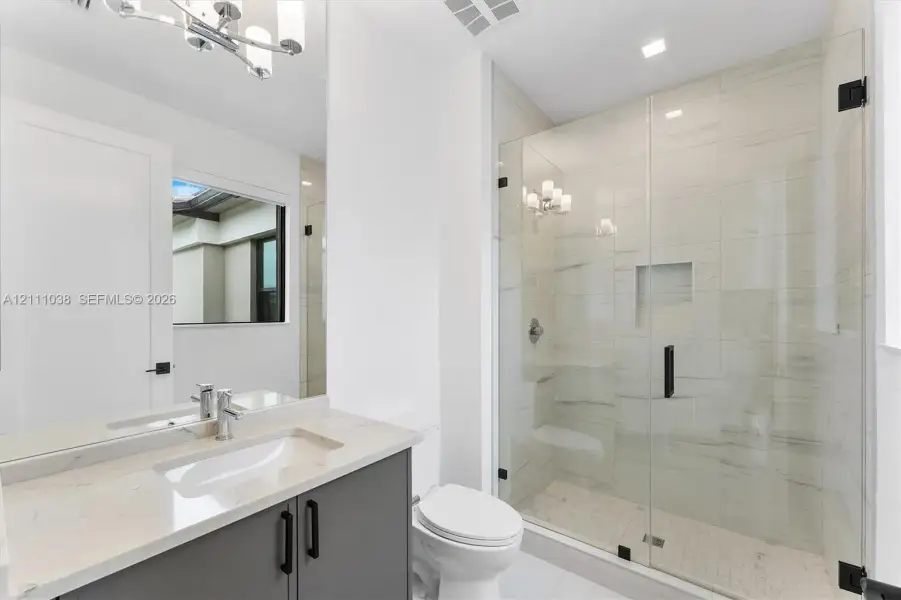 Bathroom featuring a vanity with stone-finish countertop, undermount sink, frameless glass-enclosed shower with floor-to-ceiling tile, and matte black hardware
