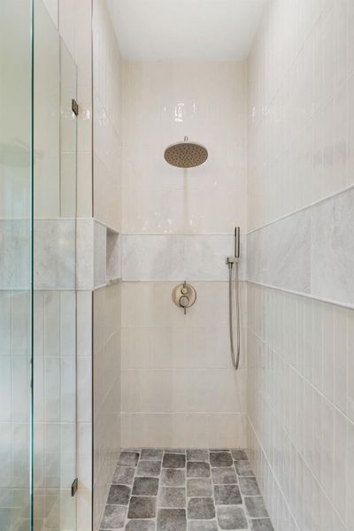 A well-appointed shower stall features a rain shower head, handheld sprayer, and stone flooring.