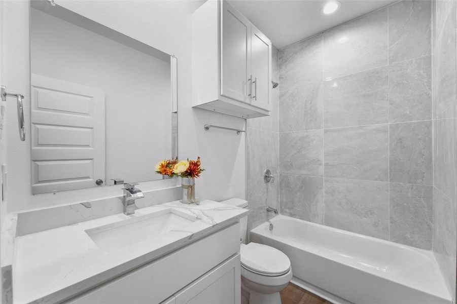 Bathroom featuring a white vanity with an integrated rectangular sink, a large wall-mounted mirror, overhead cabinetry, a toilet, and a tiled shower-bathtub combination